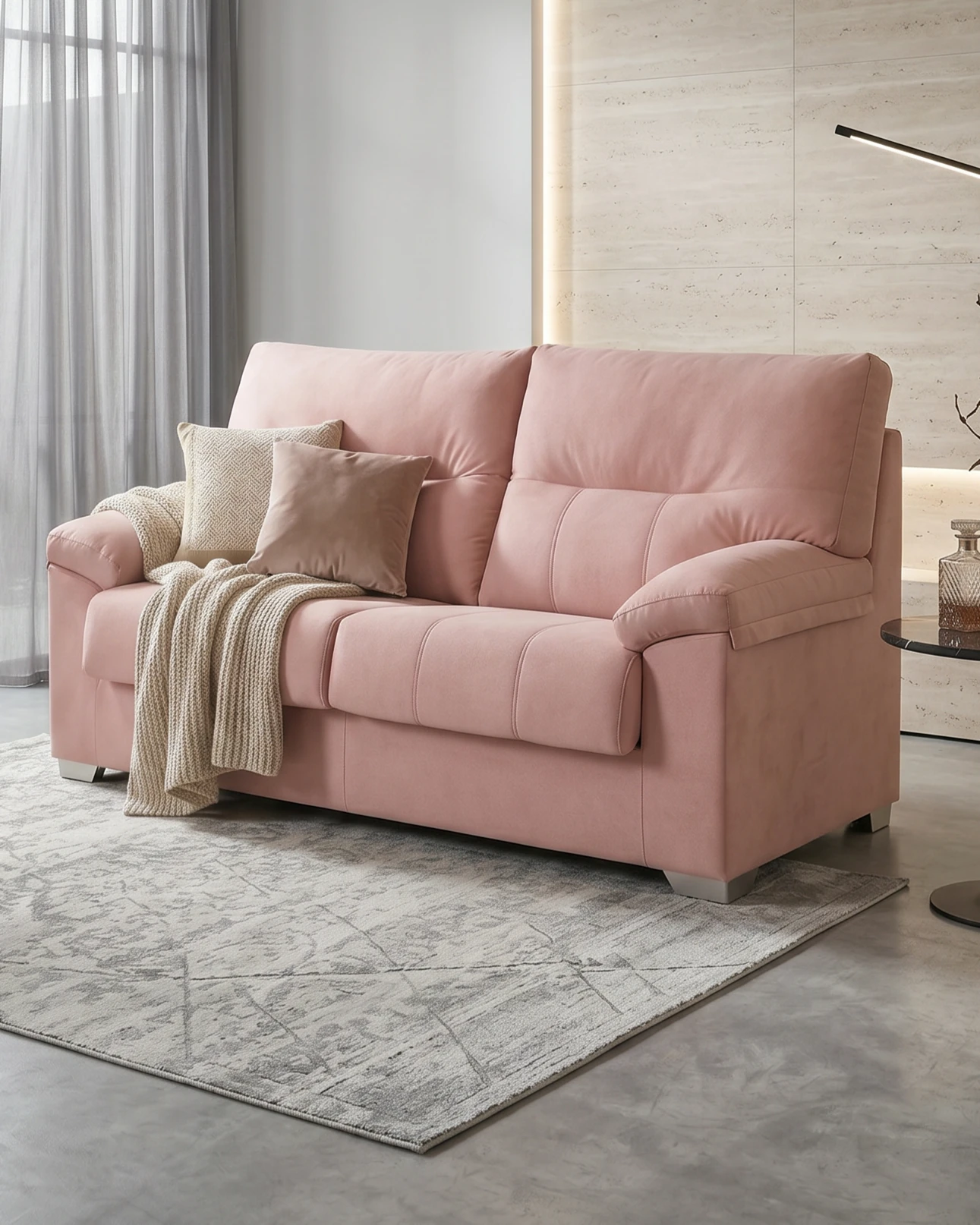 Sofa rosa claro con cojines y manta en una habitación moderna con suelo de cemento y pared de piedra